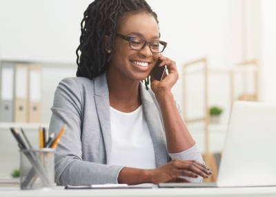 Lady Boss. Afro Businesswoman Talking On Cellphone While Working On Laptop In Modern Office, Wide Horizontal Banner, Panorama With Free Space